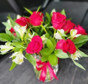 A vase filled with red roses and green leaves.